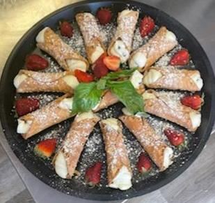 A tray of cannolis dusted with powdered sugar, with strawberries and fresh basil